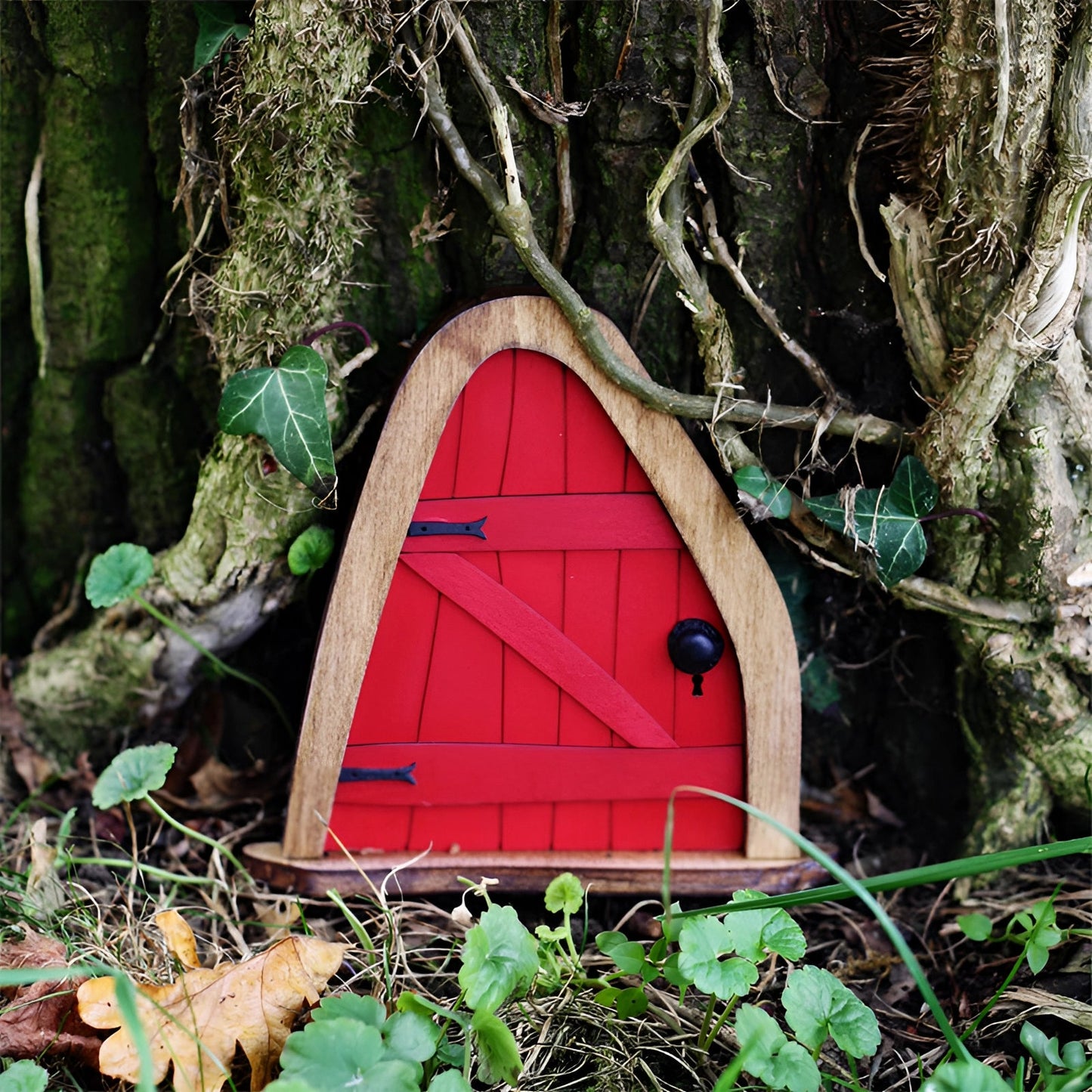 Miniature fairy garden door set against a natural landscape featuring lush green grass and various terrestrial plants, crafted to resemble an enchanted tree with intricate wood details.