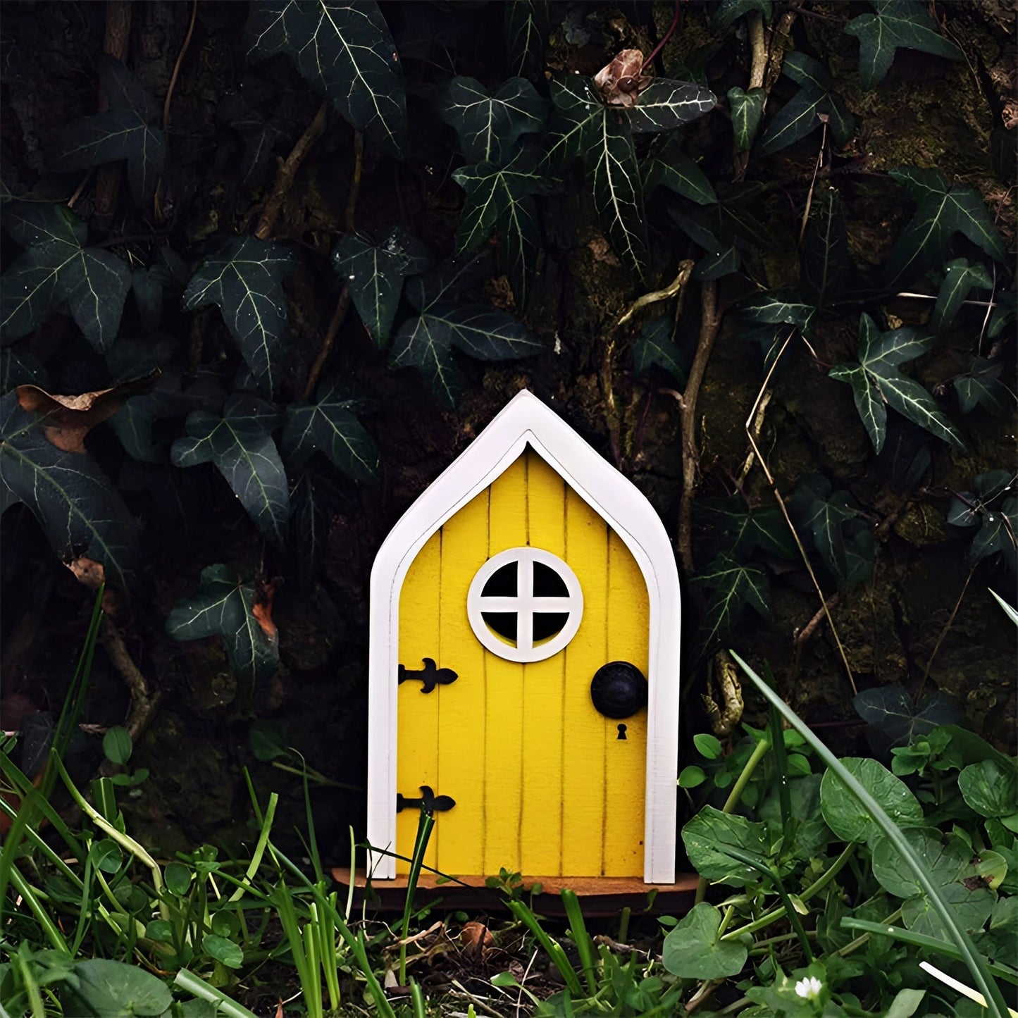 Miniature fairy garden door crafted to resemble an enchanted tree, featuring intricate wooden details, small windows, and surrounded by grass and plants.